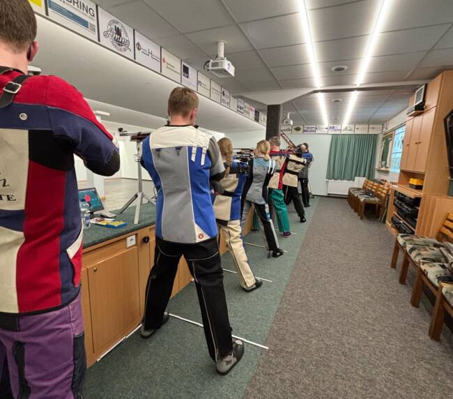 Mehrere Personen zieheln mit langwaffen auf eine Zielscheibe