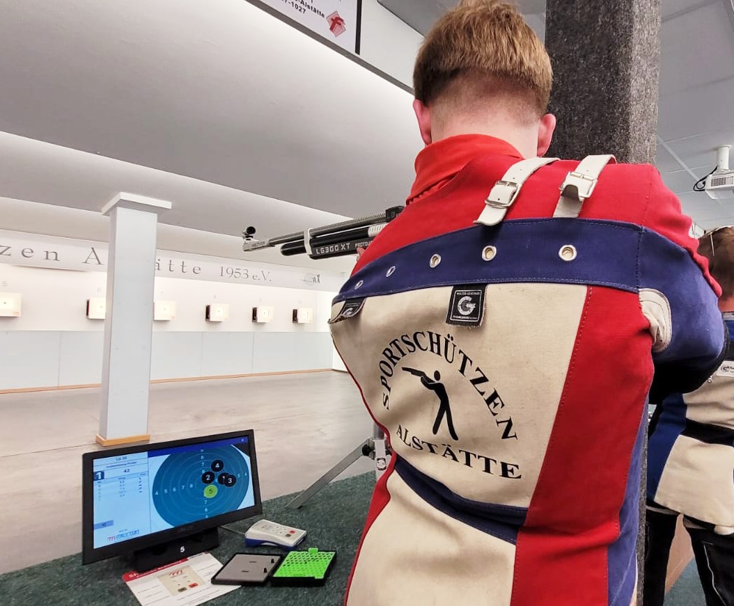 Mann schießt mit Gewehr auf Zielwand während das logo auf den Rücken im Fokus ist