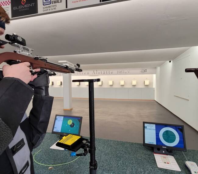 Mann zielt mit Gewähr auf eine Zielscheibe.