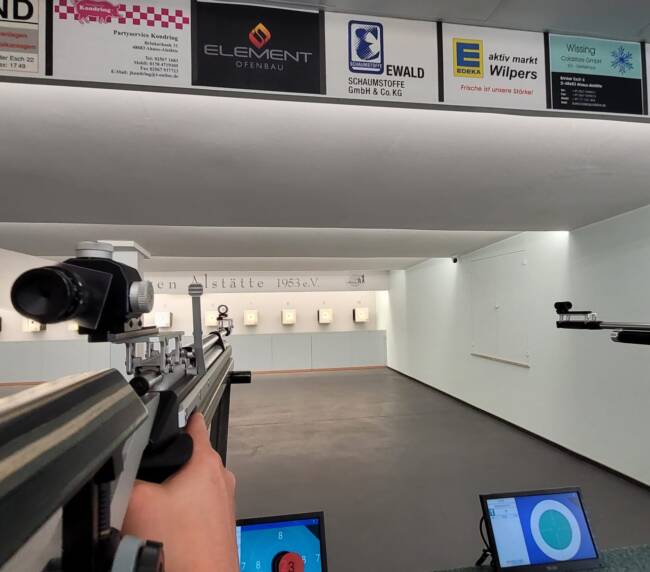 Nahaufnahme einer Langschusswaffe das auf eine Zielscheibe an einer Wand zielt