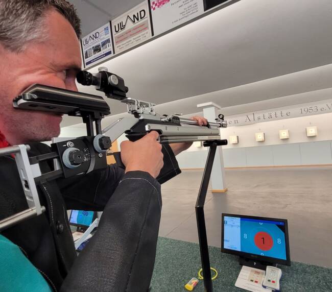 Mann zielt mit Gewähr auf eine Zielscheibe.