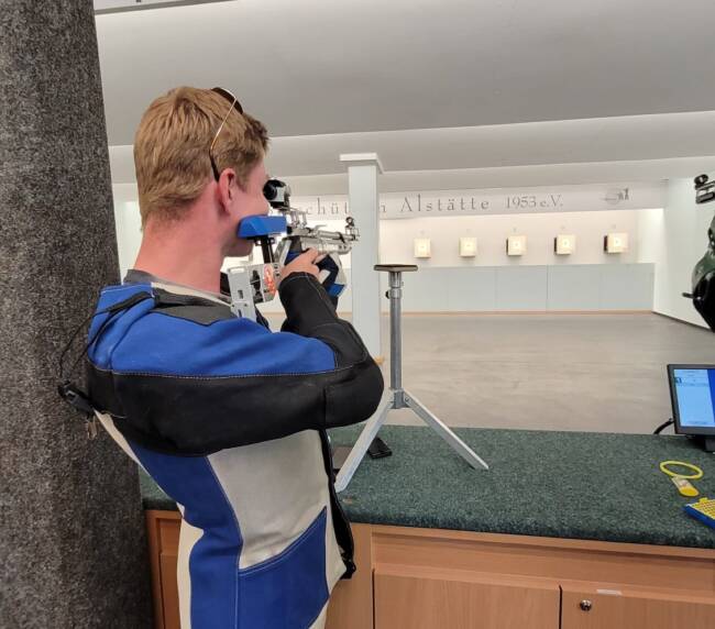 Junger Mann Zielt mit einer Lanschusswaffe auf eine Zielscheibe an einer Wand